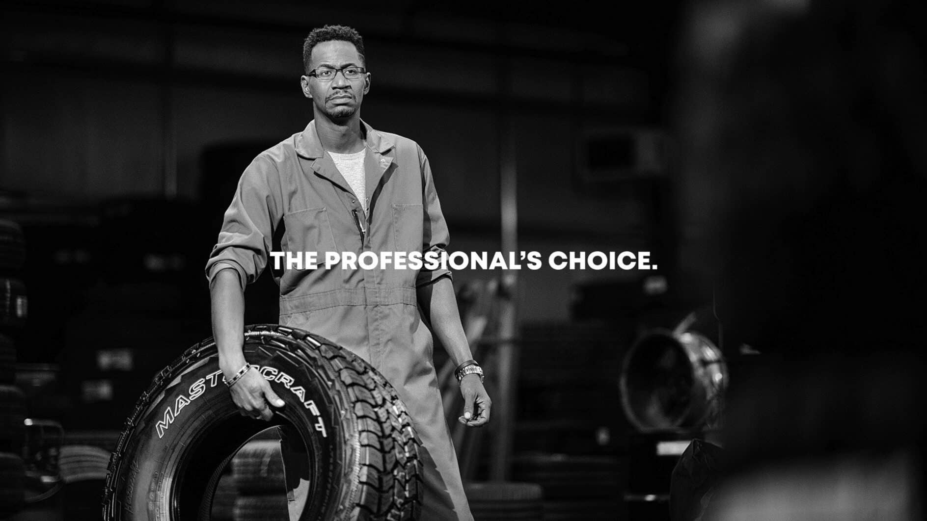 A focused mechanic in overalls holds a large tire in an industrial workshop setting. Text overlay reads "The Professional's Choice." Mood is confident and professional.