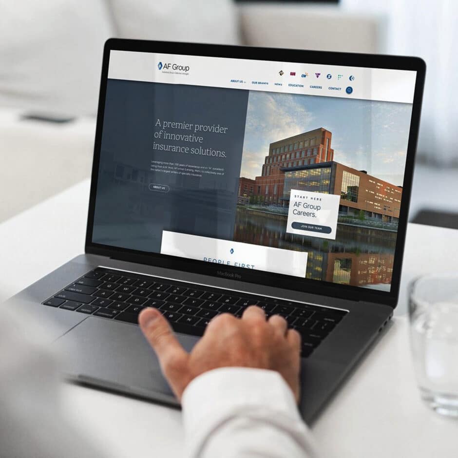 A person interacts with a laptop showing the AF Group website, featuring an insurance solutions tagline and building image. The atmosphere is professional.