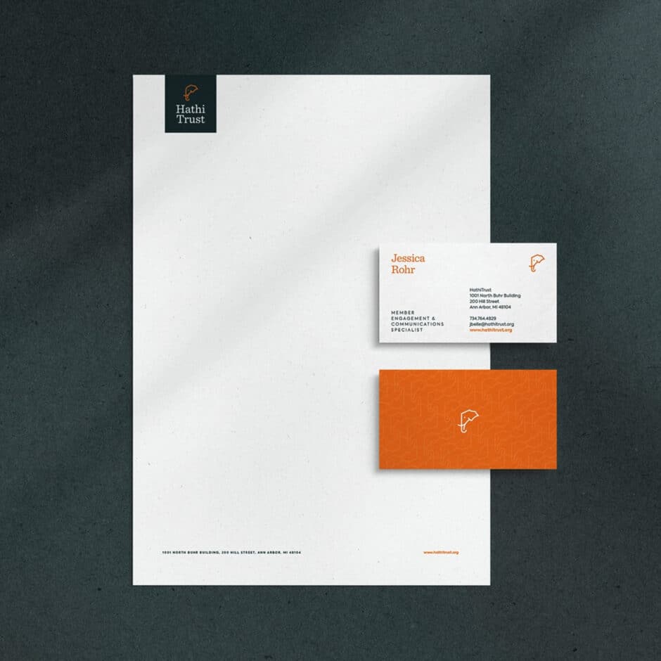 Stationery set on a dark textured surface. Includes a letterhead with "Hathi Trust" logo, a business card, and an orange card with a simple elephant icon.