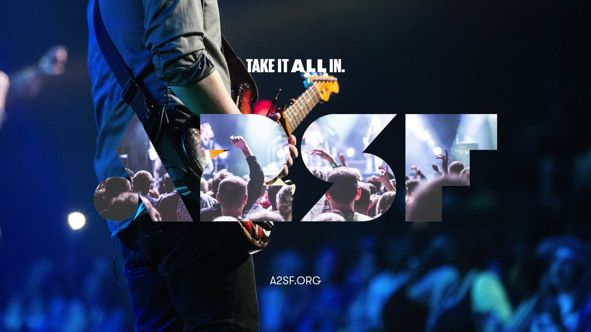 A guitarist on stage with a blue-toned, energetic crowd. "Take it all in" text overlays the scene with "A2SF" cutout, evoking excitement and engagement.