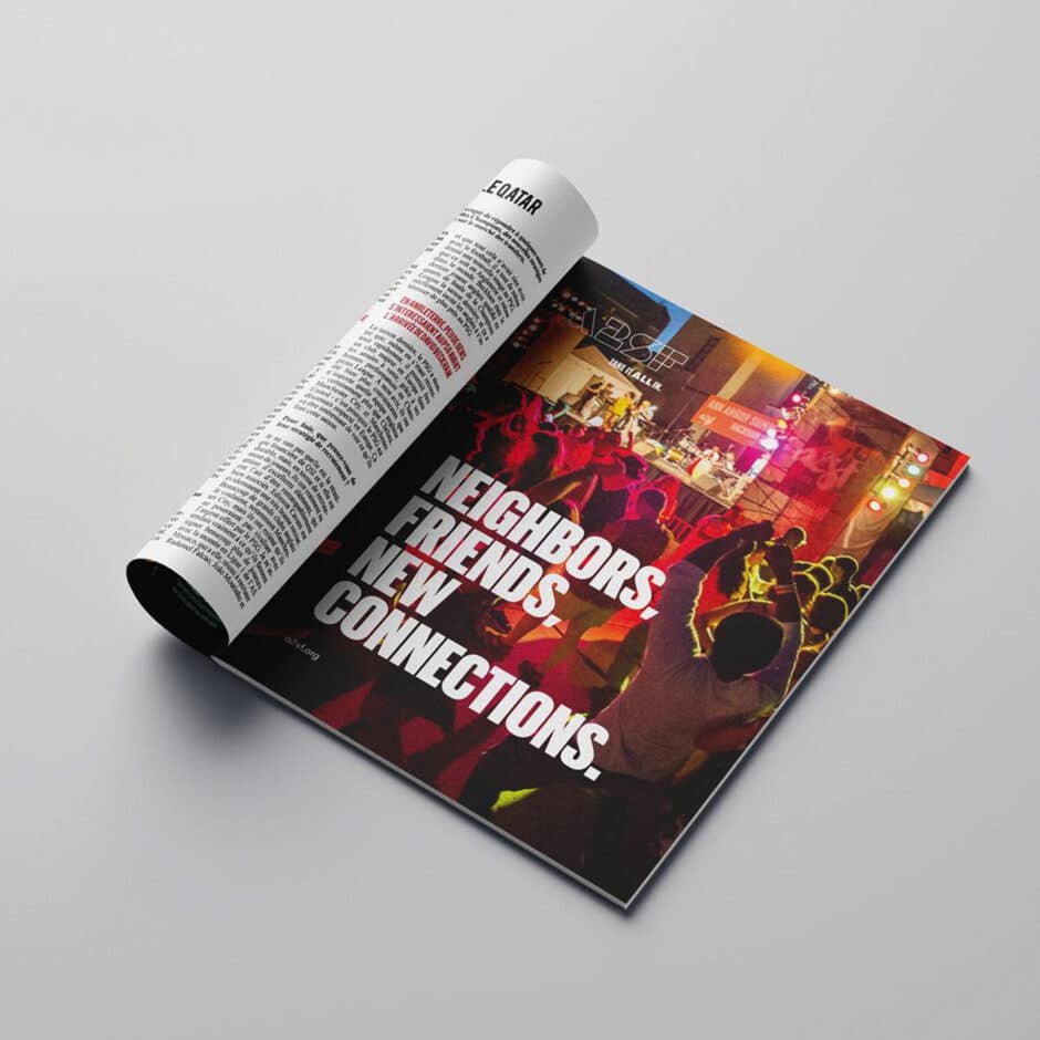 Magazine open on a flat surface, showing a lively crowd dancing under colorful lights with text: "Neighbors. Friends. New Connections."