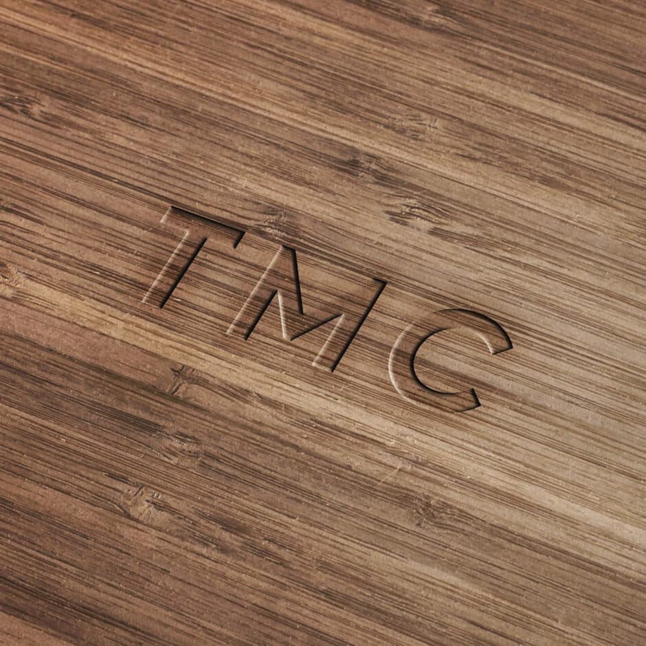 Close-up of polished wood with "TMC" etched in bold letters. The grain adds texture, conveying a natural, refined aesthetic.