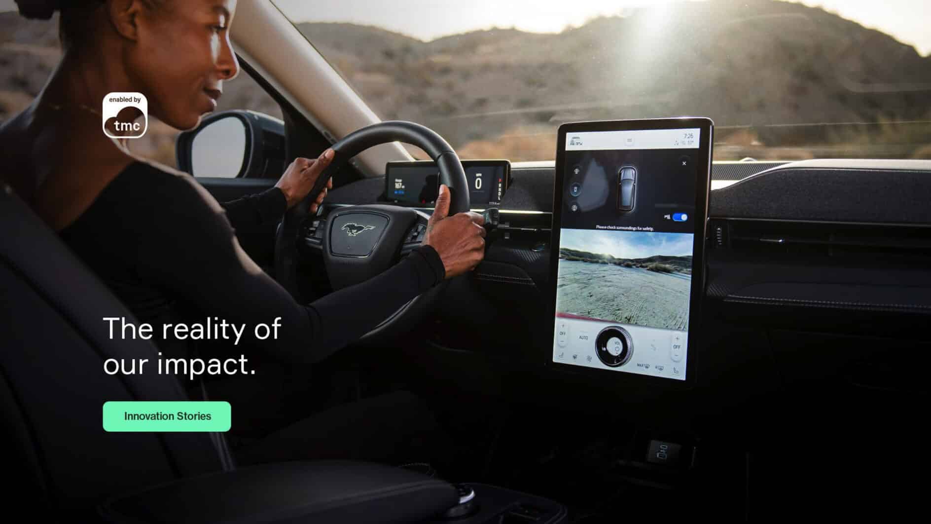 A person drives a car through a desert landscape, focusing on the road. The dashboard features a large touchscreen displaying navigation. Text reads, “The reality of our impact.”