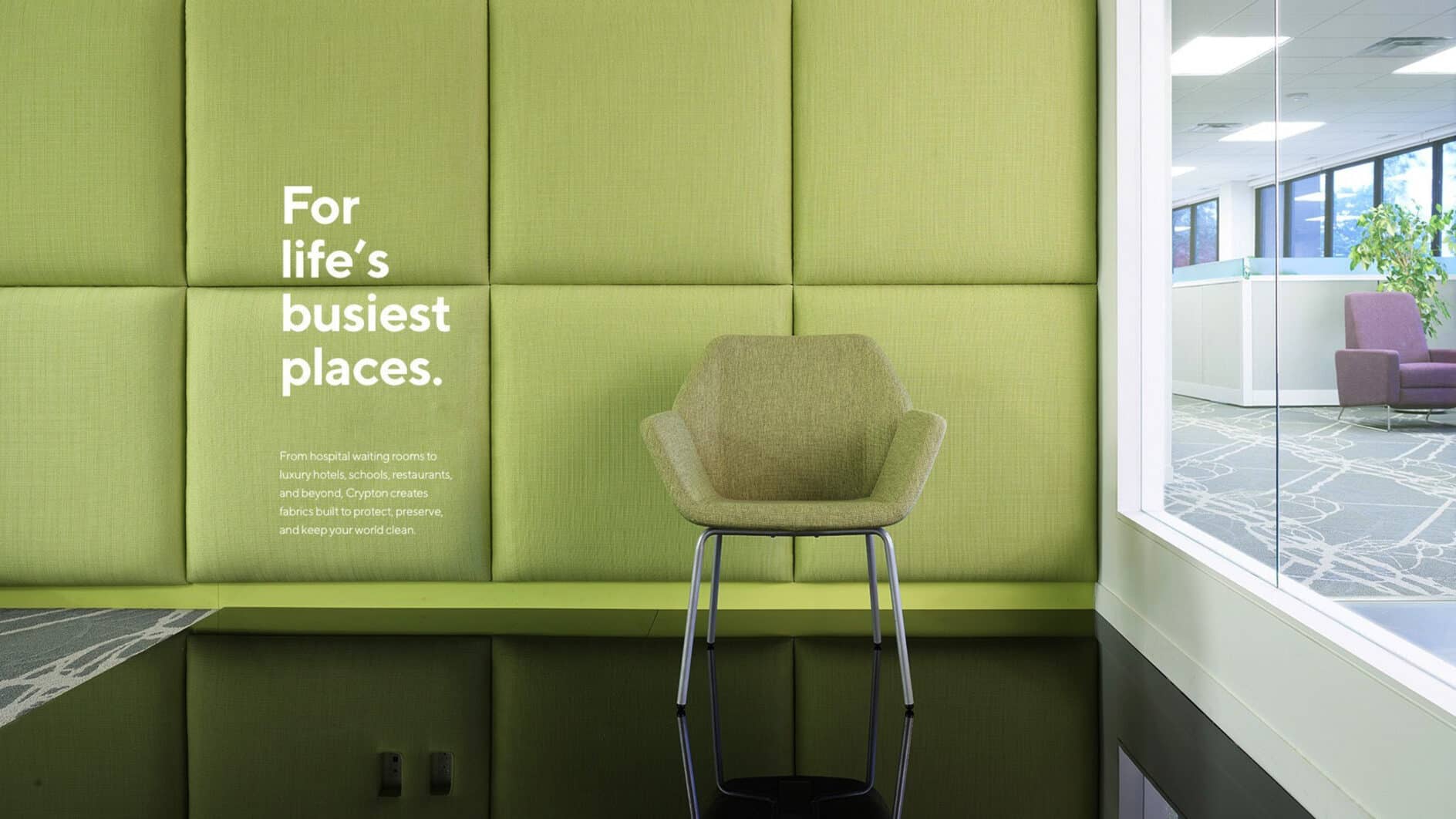 Modern office setting with a light green textured wall, a matching upholstered chair on tall legs. Bright text reads, “For life’s busiest places.” A glass window reveals a spacious office area.