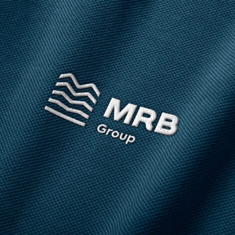 Embroidered white MRB Group logo on textured dark blue fabric; includes wavy lines and bold text, conveying professionalism and modernity.