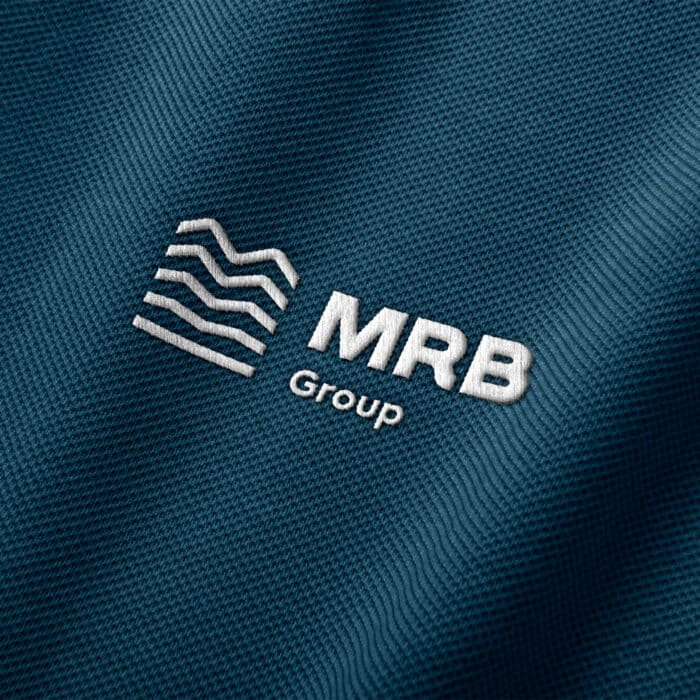 Embroidered white MRB Group logo on textured dark blue fabric; includes wavy lines and bold text, conveying professionalism and modernity.
