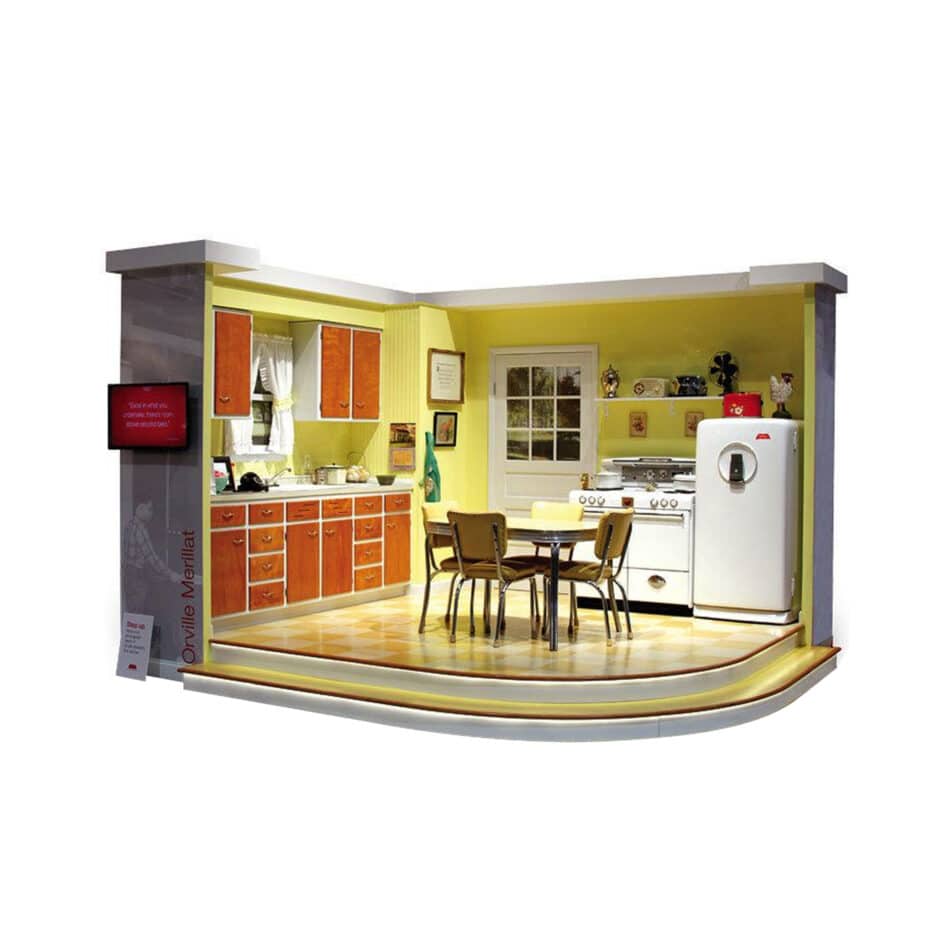 Vintage 1950s kitchen exhibit with yellow walls, wooden cabinets, a fridge, stove, and dining set. Cozy, nostalgic atmosphere with retro decor.