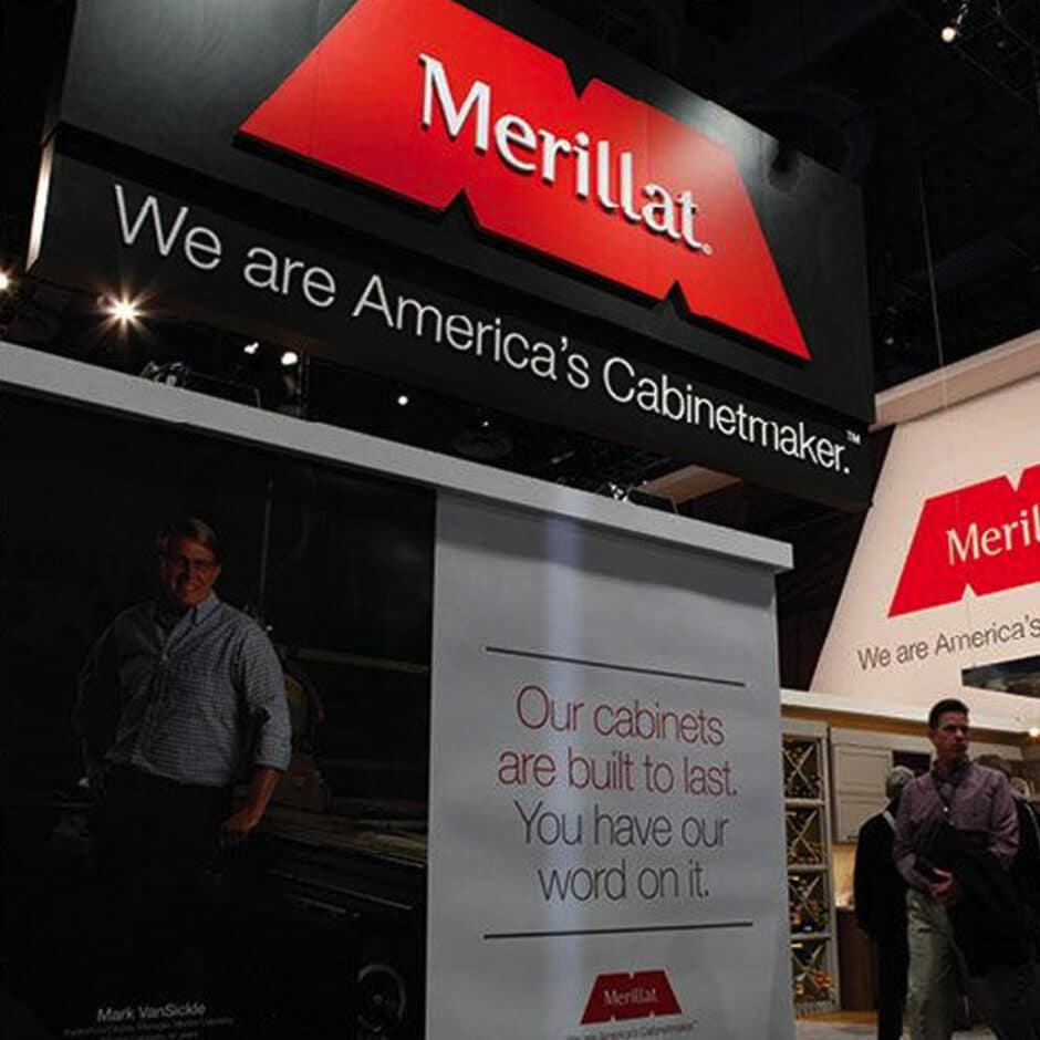 Trade show booth with a large Merillat sign and slogan "We are America's Cabinetmaker." Displays include cabinets and a poster with a smiling man.