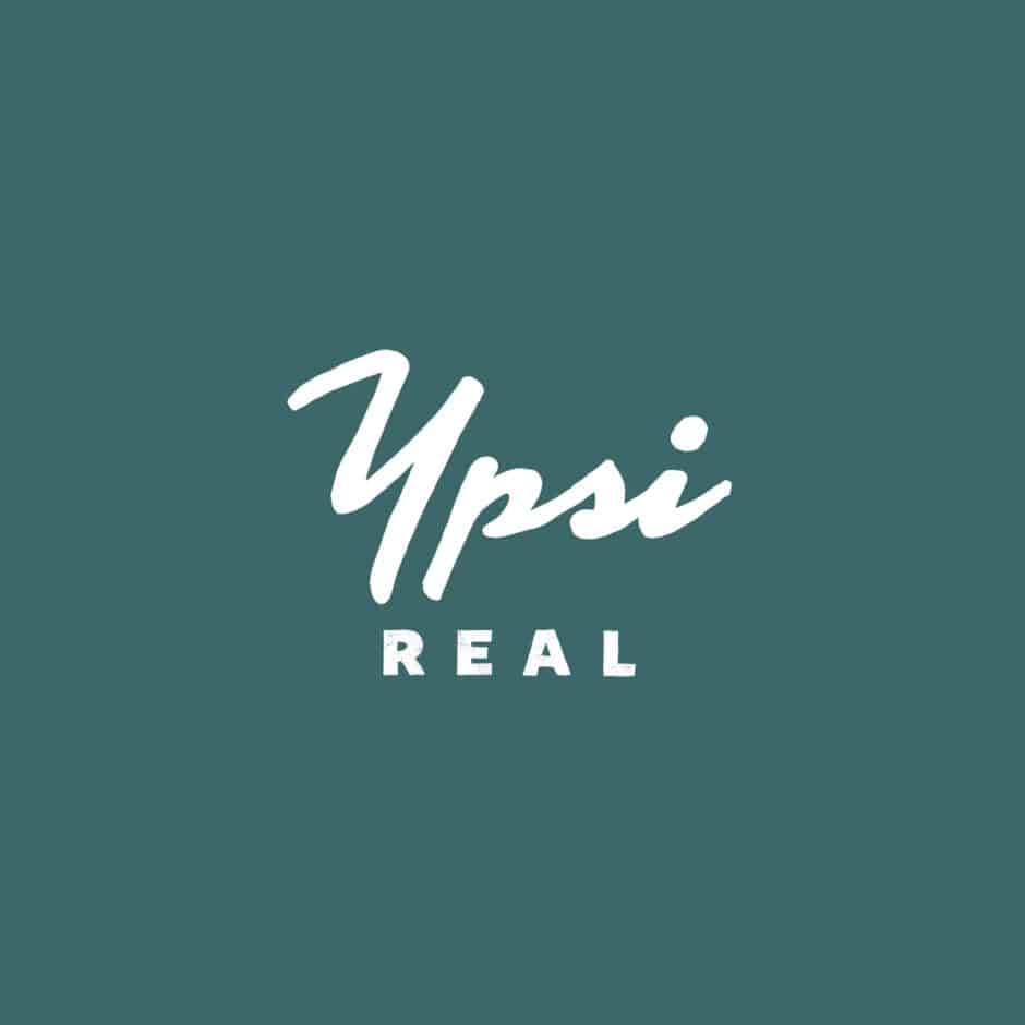The image shows the words "Ypsi Real" in white, with "Ypsi" in cursive and "REAL" in bold uppercase, set against a teal background.
