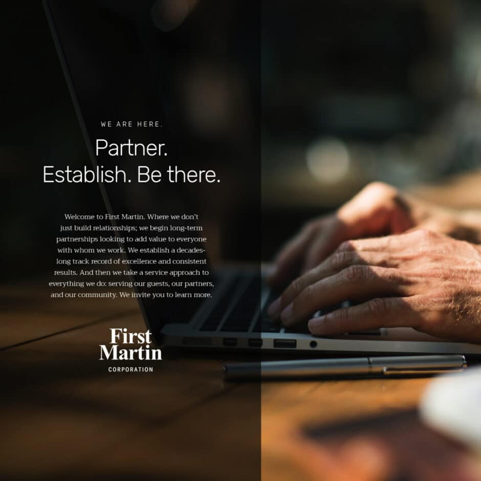 Close-up of hands typing on a laptop in a dim workspace. Overlayed text reads: "Partner. Establish. Be there." by First Martin Corporation, emphasizing collaboration.