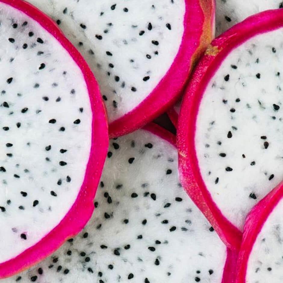 Close-up of sliced dragon fruit, showing vibrant pink rinds and white flesh speckled with small black seeds. The image highlights the fruit's exotic texture.