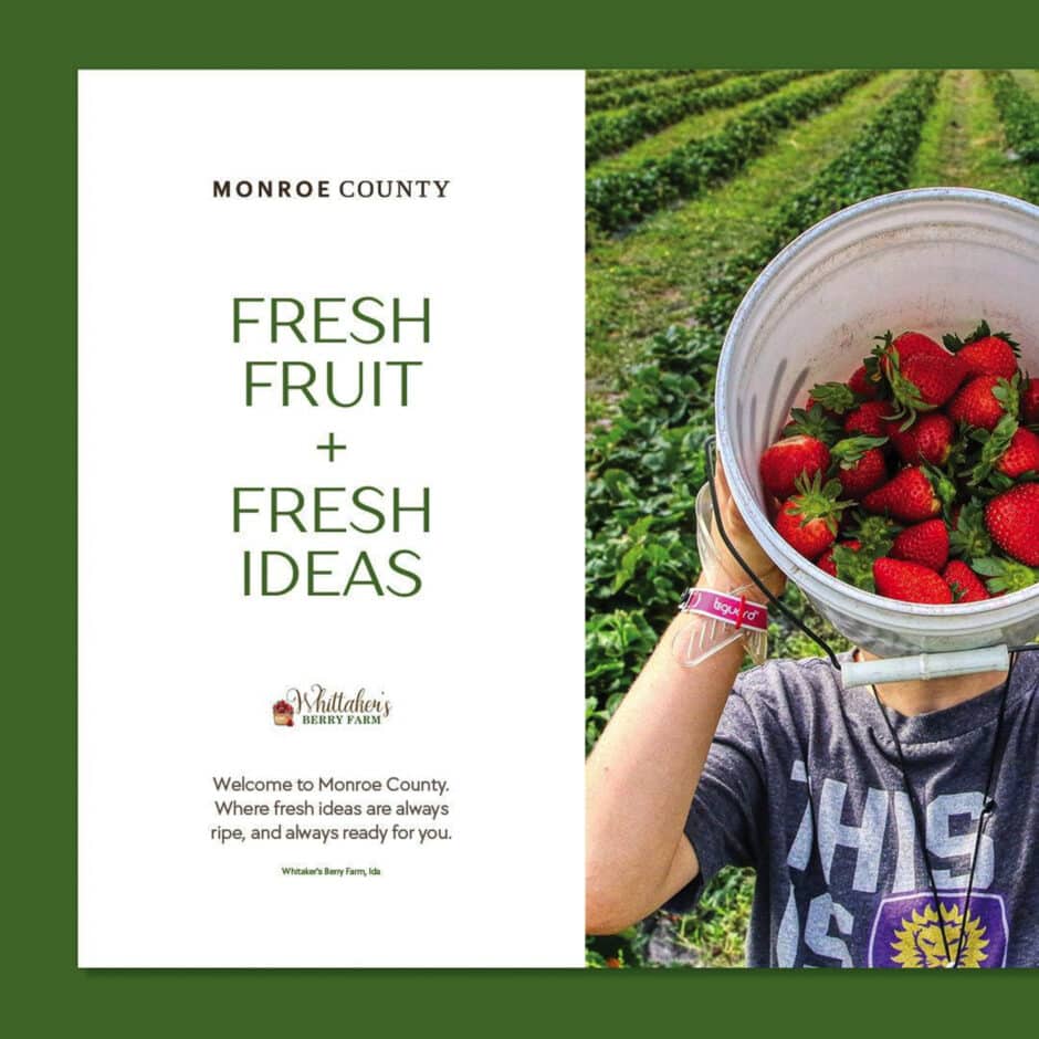 Ad for Monroe County featuring 'Fresh Fruit + Fresh Ideas'. Right shows person holding bucket of red strawberries in a field. Whittaker's Berry Farm logo included.