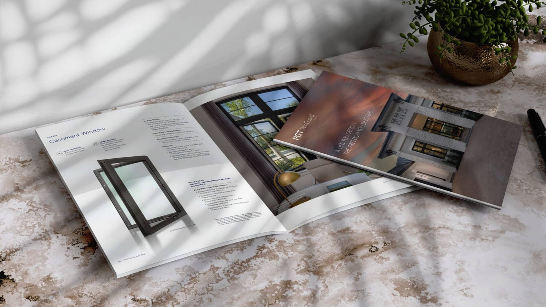 Open brochures on a marble surface show modern window designs. Soft shadows and a plant add a calm, stylish atmosphere. Pen nearby.