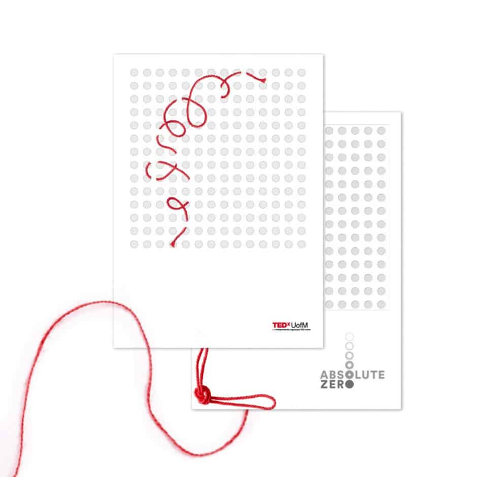 White card with circular perforations arranged in a grid. Red thread loops through the holes, forming a pattern. "TEDxUofM" and "ABSOLUTE ZERO" are printed.