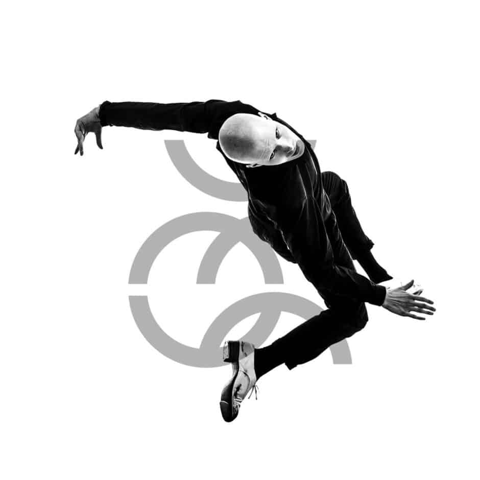 Bald dancer dynamically leaps, mid-air in black attire, exuding grace against a white backdrop with abstract circular gray design elements.