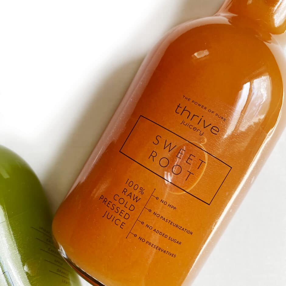 Orange juice bottle labeled "Thrive Juicery Sweet Root, 100% Raw Cold Pressed Juice" with no preservatives or additives. Energetic and fresh vibe.