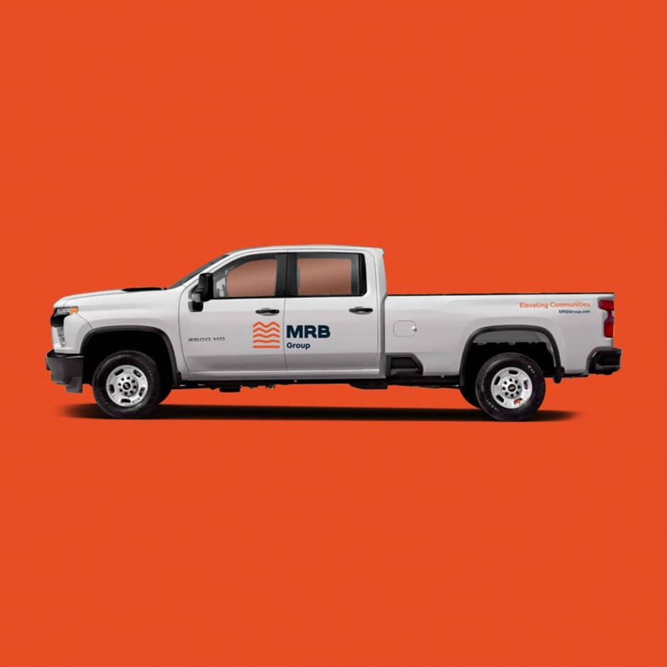 A white pickup truck with "MRB Group" logo on the door is set against an orange background. The truck is facing left, conveying professionalism and reliability.