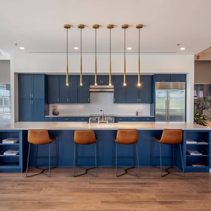 Modern kitchen with blue cabinetry, white countertops, and chevron backsplash. Features brown leather barstools, pendant lights, and wood flooring.