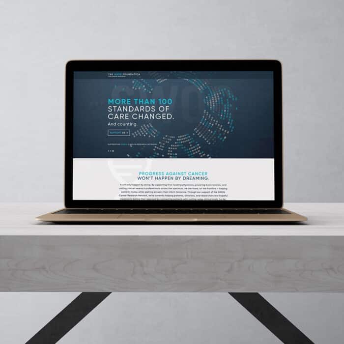 A laptop on a wooden desk displays a website with dark blue background and text: "More than 100 standards of care changed." Tone is professional and hopeful.