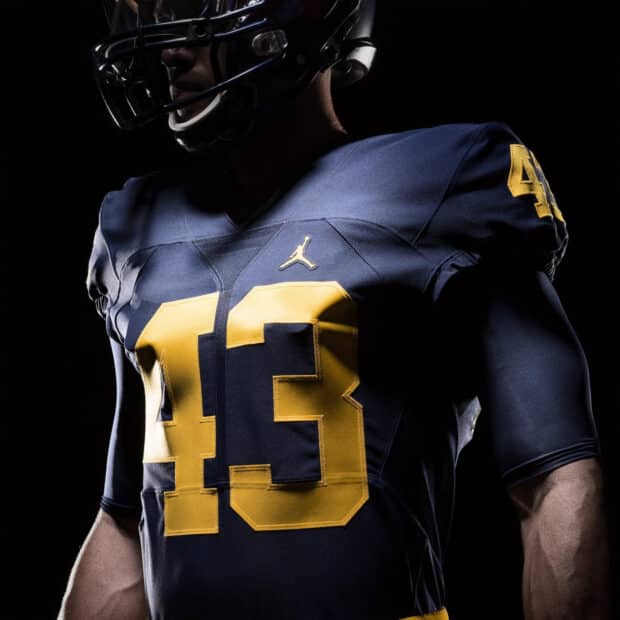 Football player in a navy and yellow uniform with number 43, partially lit against a dark background. The attire features a small Jumpman logo, creating a strong, focused tone.