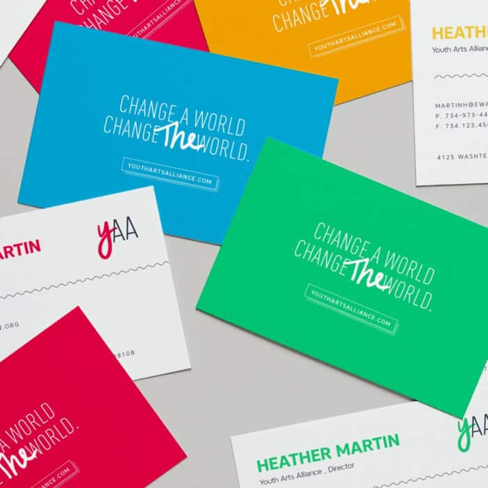 Colorful business cards scattered on a gray surface, with bold messages like "Change a World, Change the World" in dynamic fonts, conveying energy and inspiration.