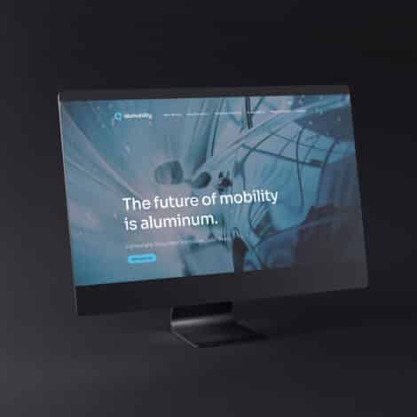 Computer screen displaying a webpage with a blurred car image in motion, text reads "The future of mobility is aluminum," conveying innovation and speed.
