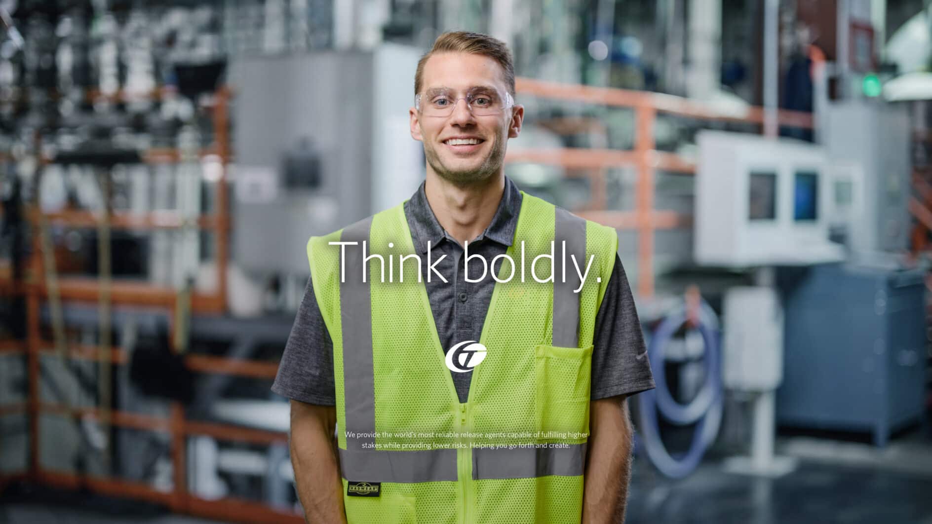 A man in a yellow safety vest and glasses stands in a factory, smiling confidently. The words "Think boldly" are in the foreground, conveying a message of innovation.