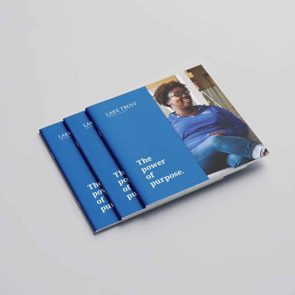 Stacked brochures with a blue cover featuring the text "The power of purpose." A smiling person in casual attire is visible on the right side.