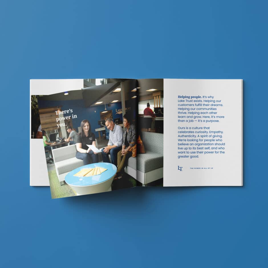 An open brochure on a blue surface shows three people collaborating, with text reading "There's power in you." The right page discusses empowering communities and empathy.