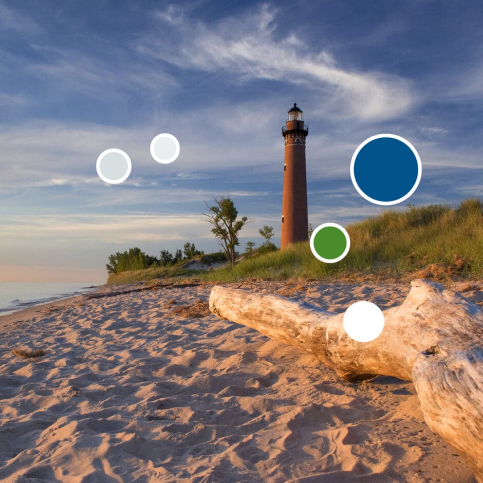 A tall lighthouse stands near sandy dunes and calm water under a vibrant sky. Driftwood rests on the shore, conveying a serene, coastal vibe.