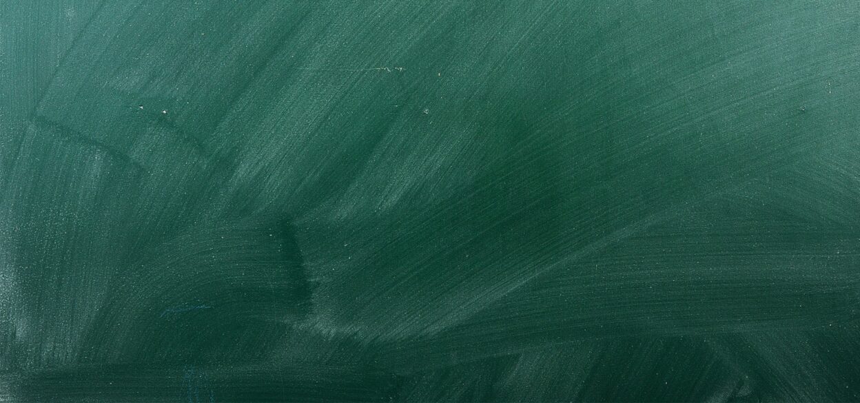 A green chalkboard with visible chalk smudges and streaks, creating a textured background. The surface appears clean but slightly worn, evoking a classroom setting.