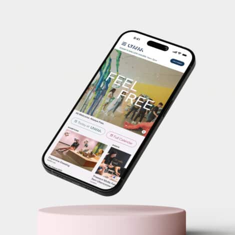 Smartphone displaying a gallery website with the words “Feel Free” over an art exhibit image. The screen shows upcoming events. Phone hovers above a pink pedestal.