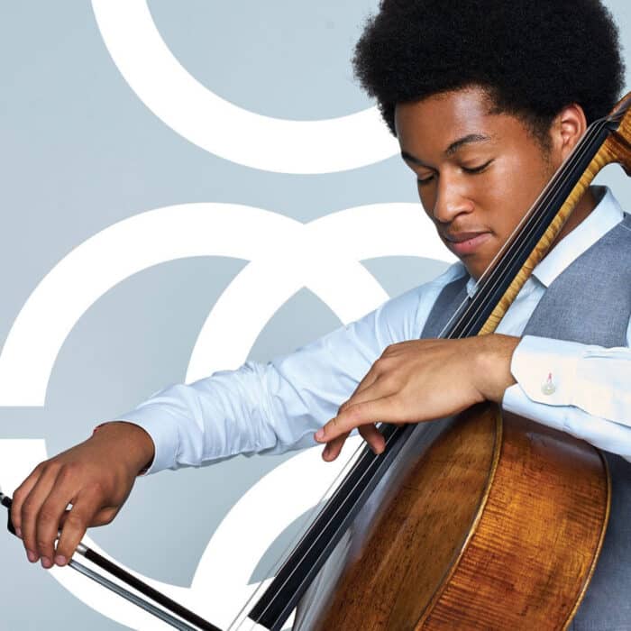 Man with an afro hairstyle playing a cello, wears a light blue shirt and gray vest. He is focused, with a serene expression against a light blue background with white circles.