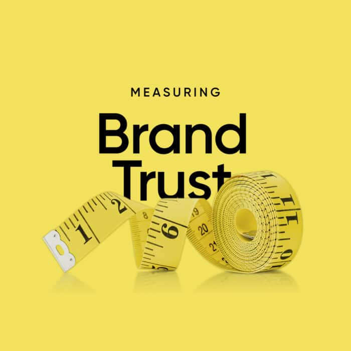 Yellow measuring tape rolled and curved on a bright yellow background. Black text reads "Measuring Brand Trust," conveying evaluation and reliability.