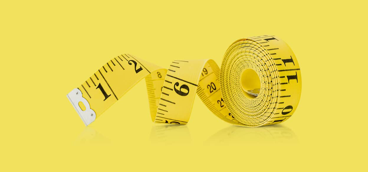 A yellow measuring tape, partially unrolled, lies on a matching yellow surface. The bold black numbers and increments are clearly visible, creating a crisp and vibrant look.