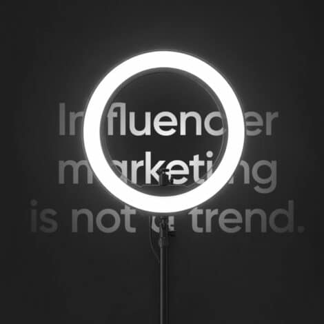 A bright ring light on a stand illuminates the words "Influencer marketing is not a trend" on a dark background, conveying a bold, modern message.
