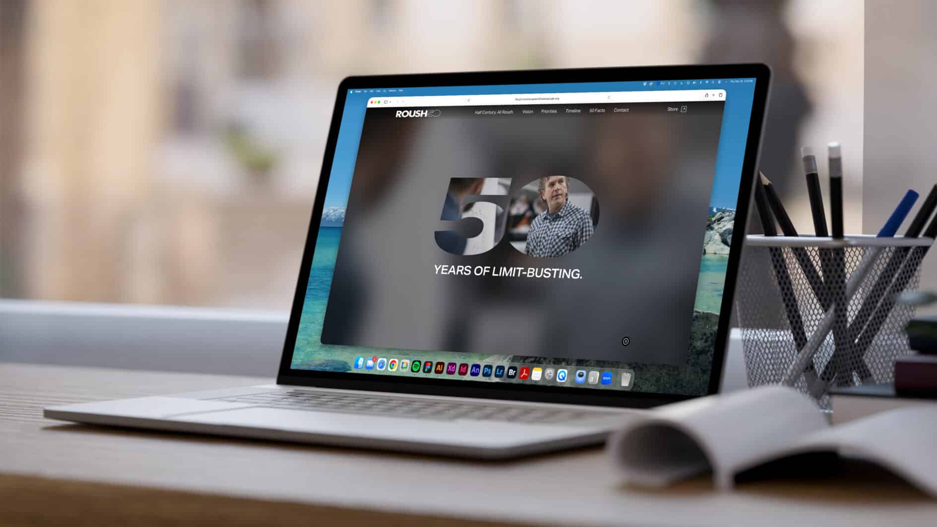 A laptop on a desk displays a website celebrating "50 Years of Limit-Busting." The screen shows a blurred background with a focus on the text.