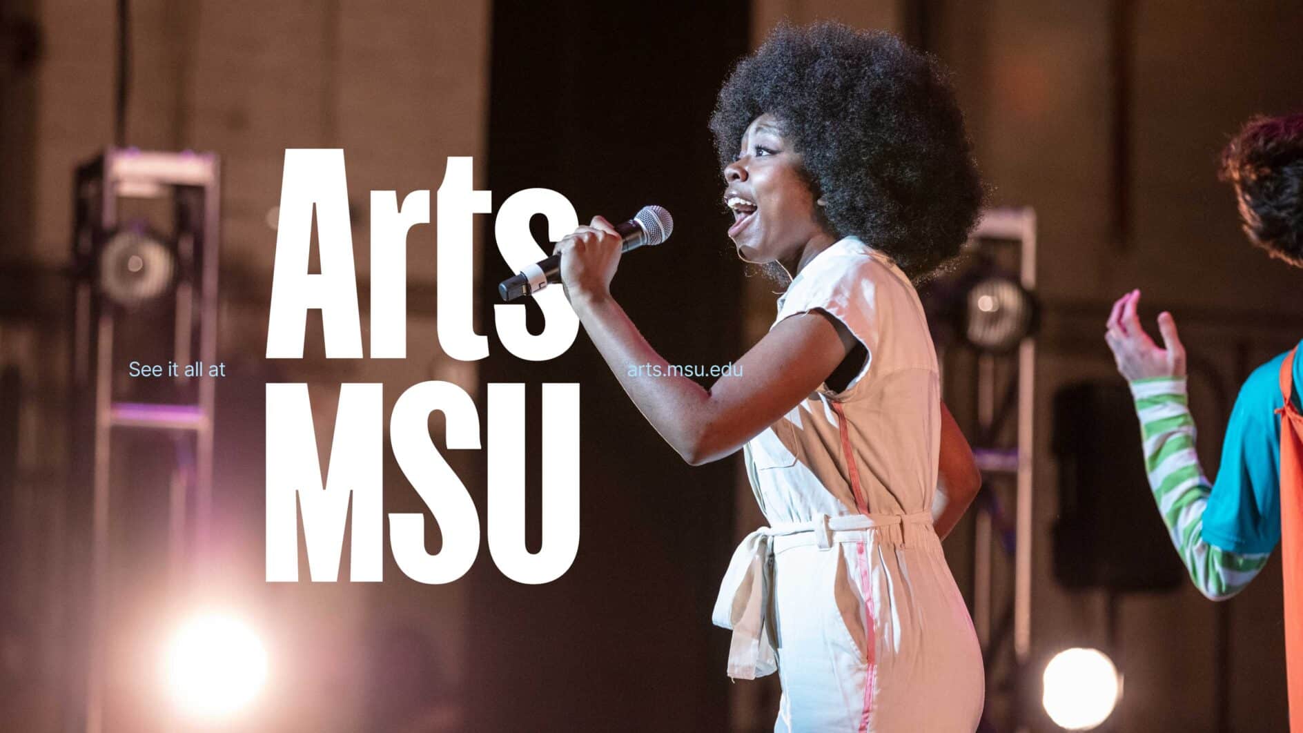 A singer passionately performs on stage, microphone in hand, wearing a light-colored jumpsuit. Bright stage lights and blurred figures create an energetic atmosphere. Arts MSU logo alongside "See it all at arts.msu.edu".