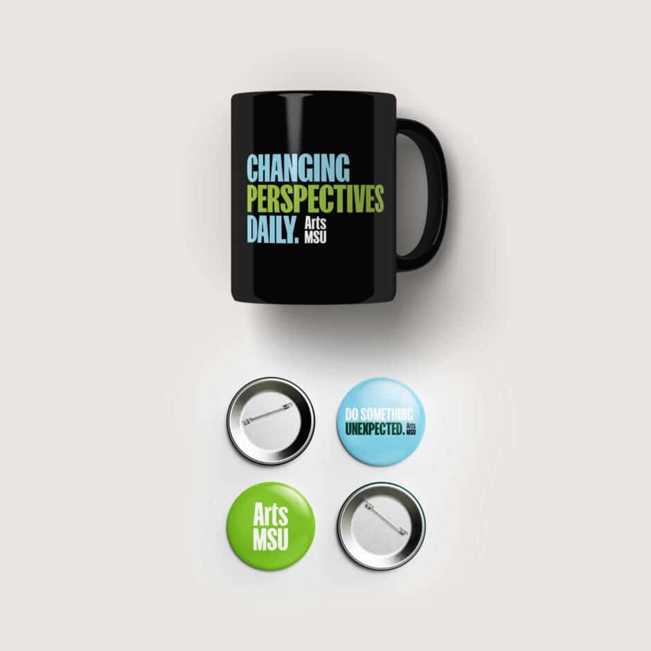 Black mug with "Changing Perspectives Daily" in blue and green text and the Arts MSU logo in white. Below, are four buttons that say "Arts MSU" and "Do Something Unexpected."