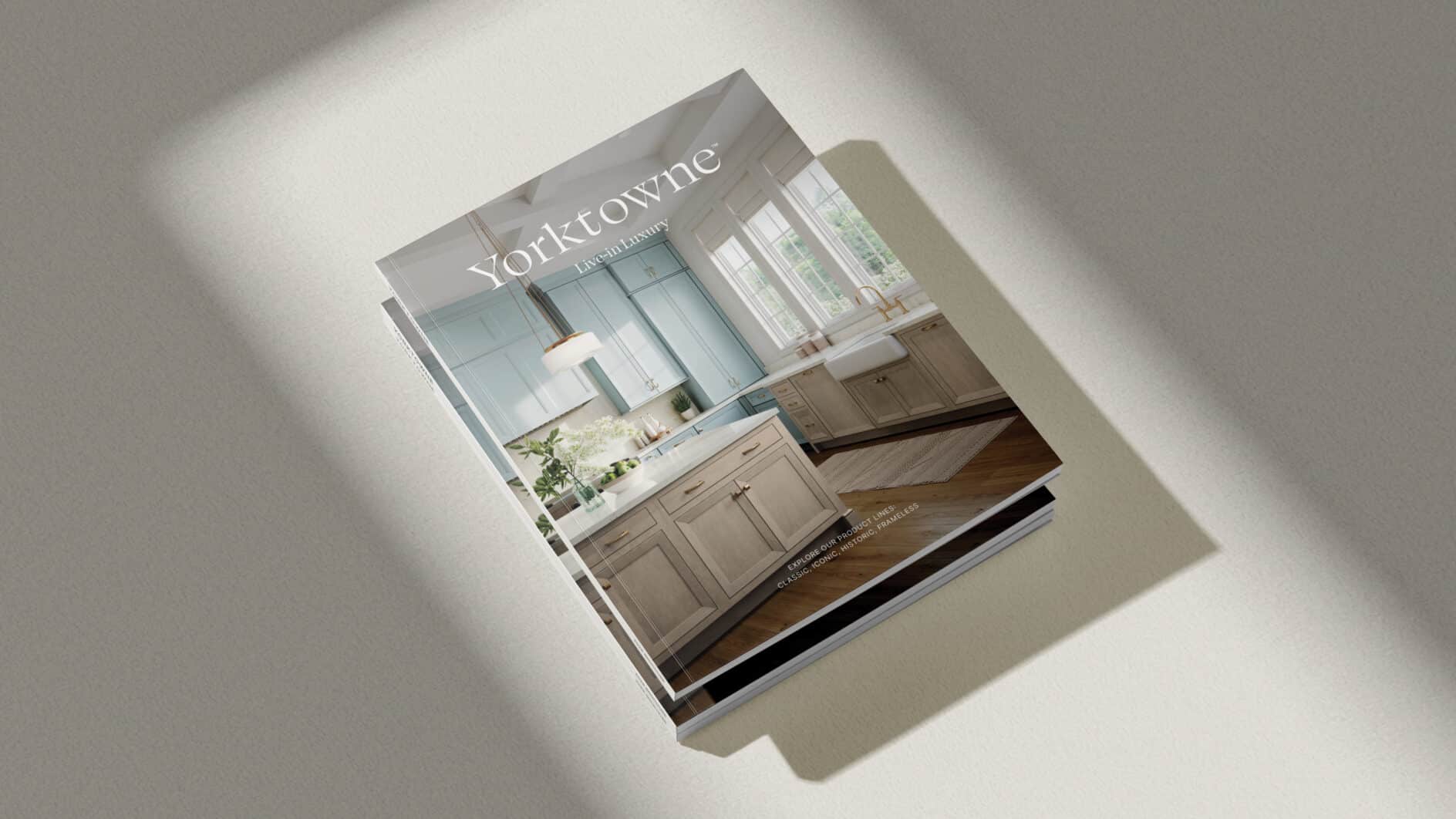 A catalog cover titled "Yorktowne" featuring a bright kitchen with light blue cabinetry, white countertops, large windows, and a cozy, elegant ambiance.