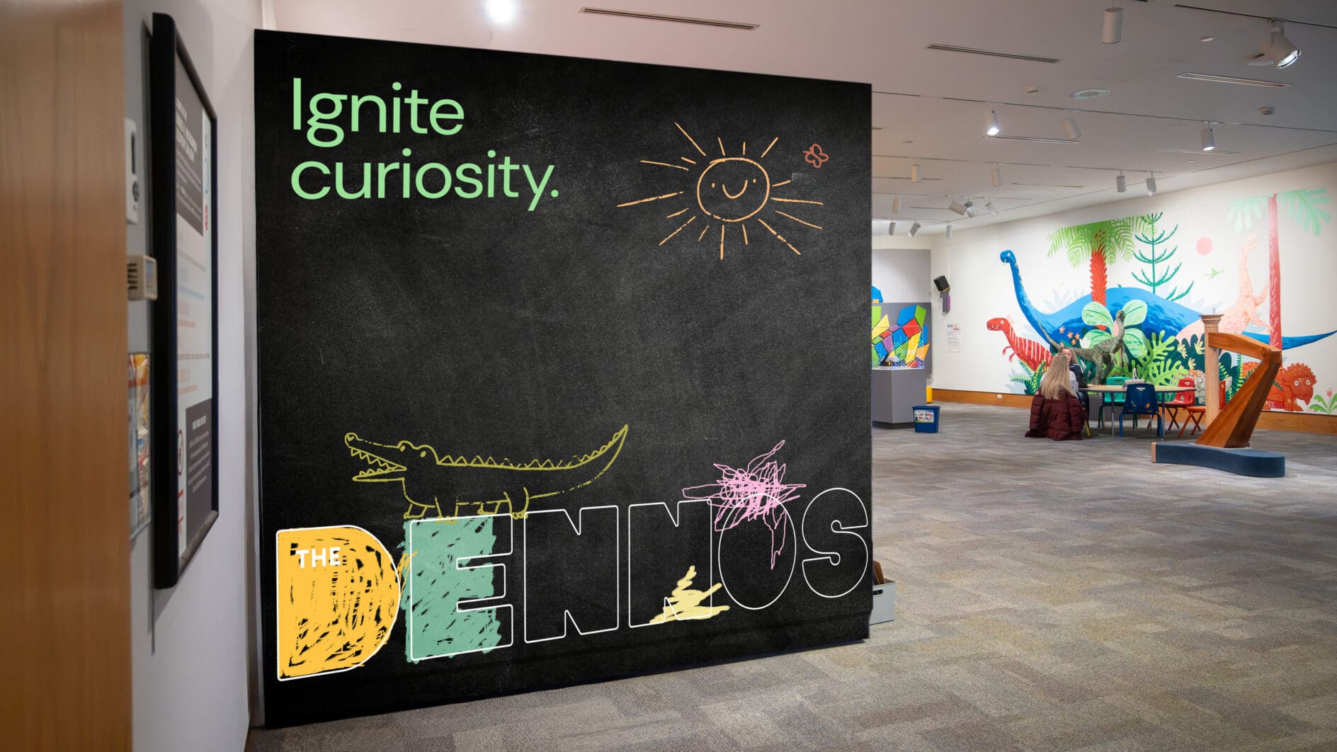 A black museum sign reads “Ignite curiosity” above a chalk sun and colorful “DINOS” lettering, with a bright dinosaur exhibit beyond.
