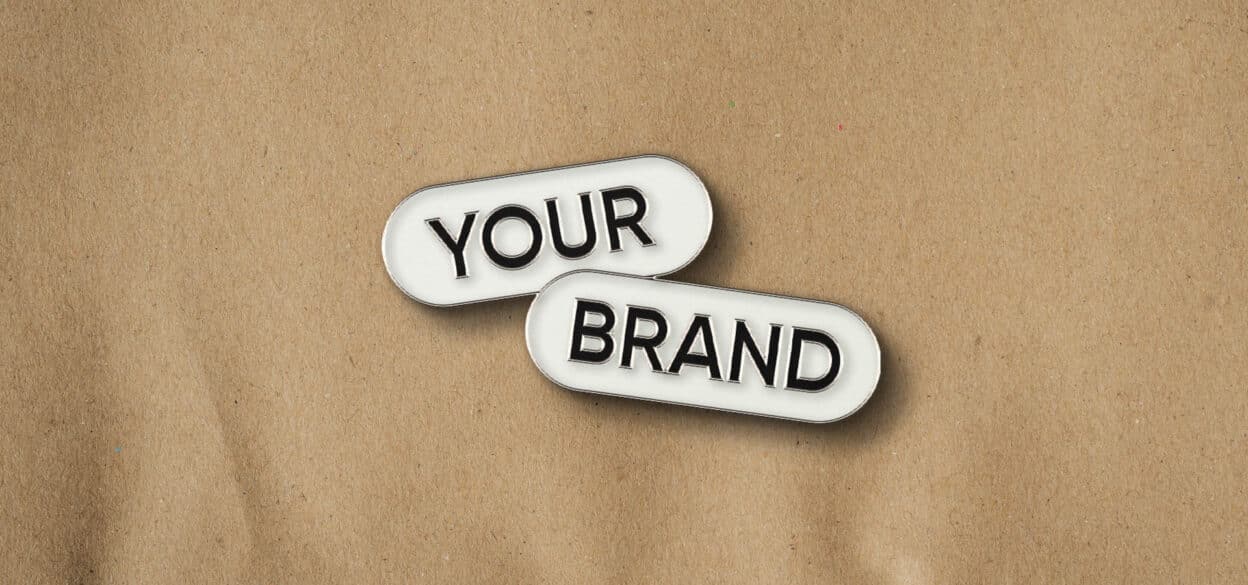Two white, rounded label tiles reading “YOUR” and “BRAND” overlap on a textured tan background, conveying a simple, professional branding message.