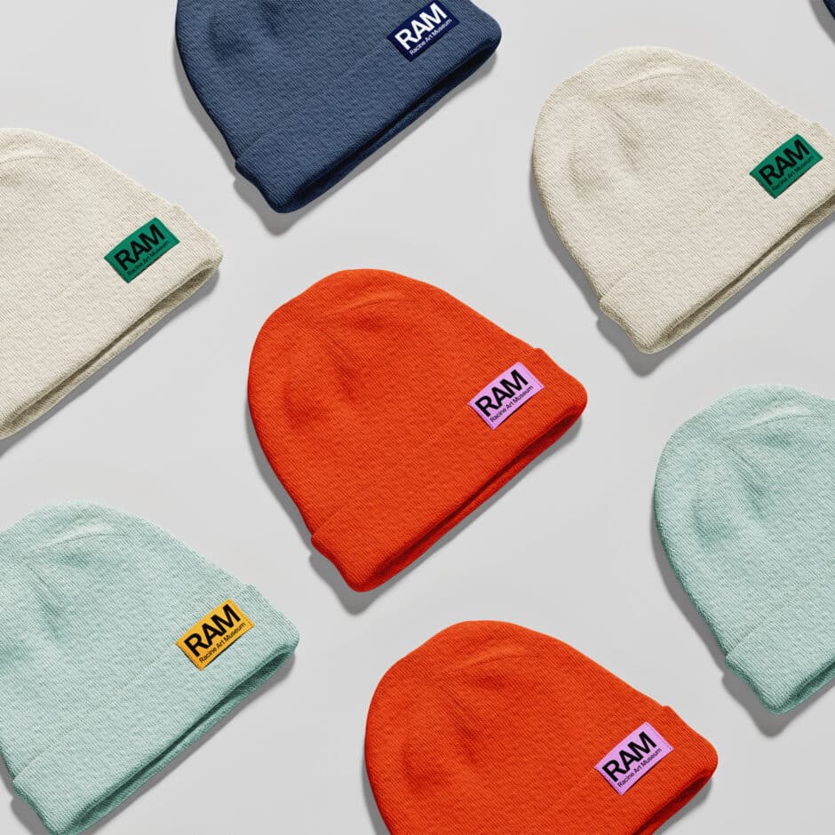 Colorful knit beanies in orange, navy, cream, and mint with RAM logo patches arranged on a gray background, creating a playful product display.