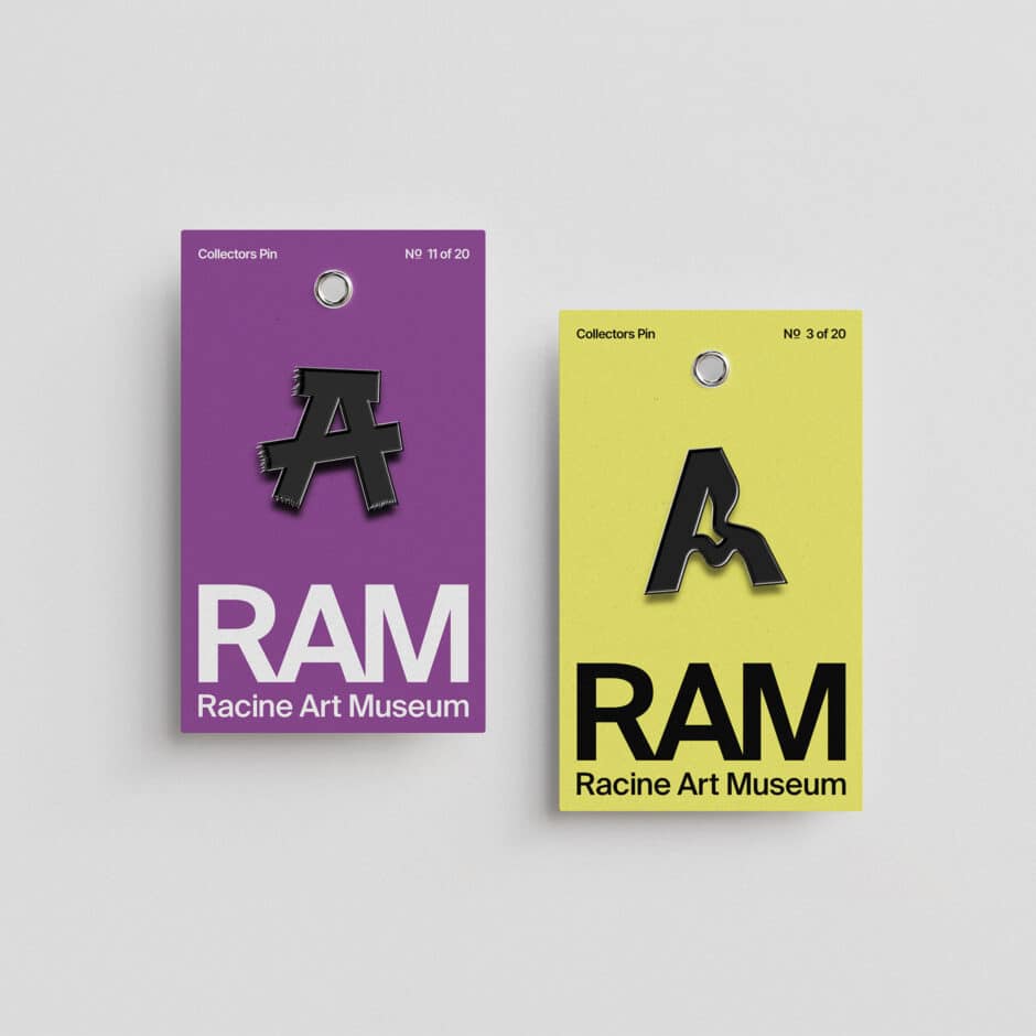 Two Racine Art Museum collector pins on gray: purple and yellow cards feature stylized black “A” logos and bold RAM lettering.