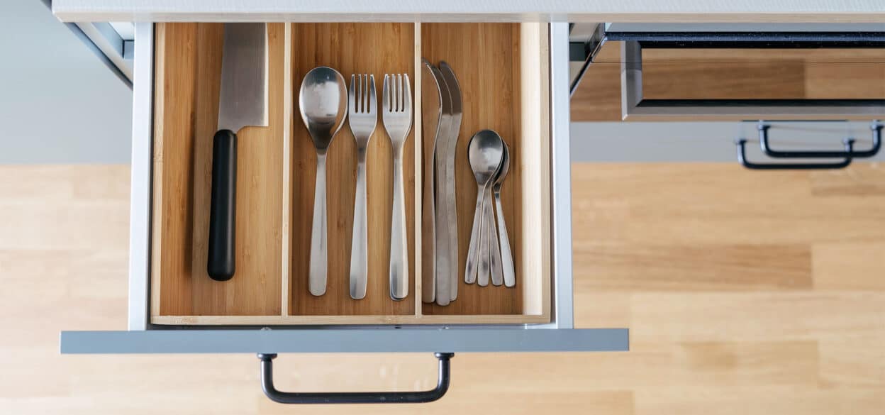 Top-down view of an open wooden kitchen drawer neatly organizing knives, spoons, forks, and utensils in a compartment tray; clean and orderly.